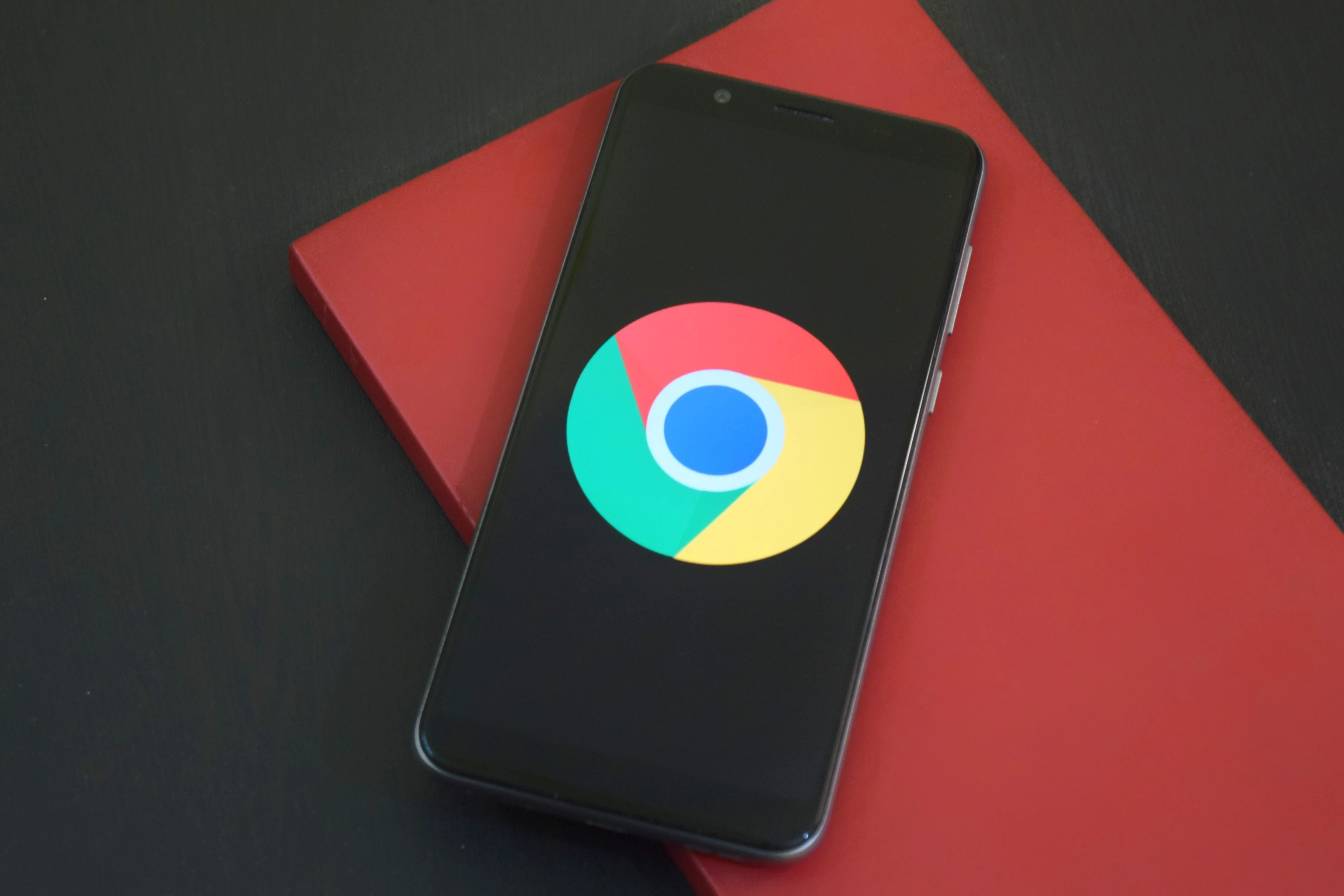 A smartphone displaying the Google Chrome logo on a red notebook.